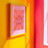 Retro-style poster with psychedelic 1970s-inspired design. Text reads "WEIRD GIRLS DO IT BETTER" in wavy, groovy lettering. Pink and orange sunburst background. Centered text surrounded by curved rays. Bold red frame with scalloped edges. Vibrant colors and playful typography create a vintage hippie vibe. Square format print with rounded corners. Perfect for fans of retro aesthetics and empowering slogans.